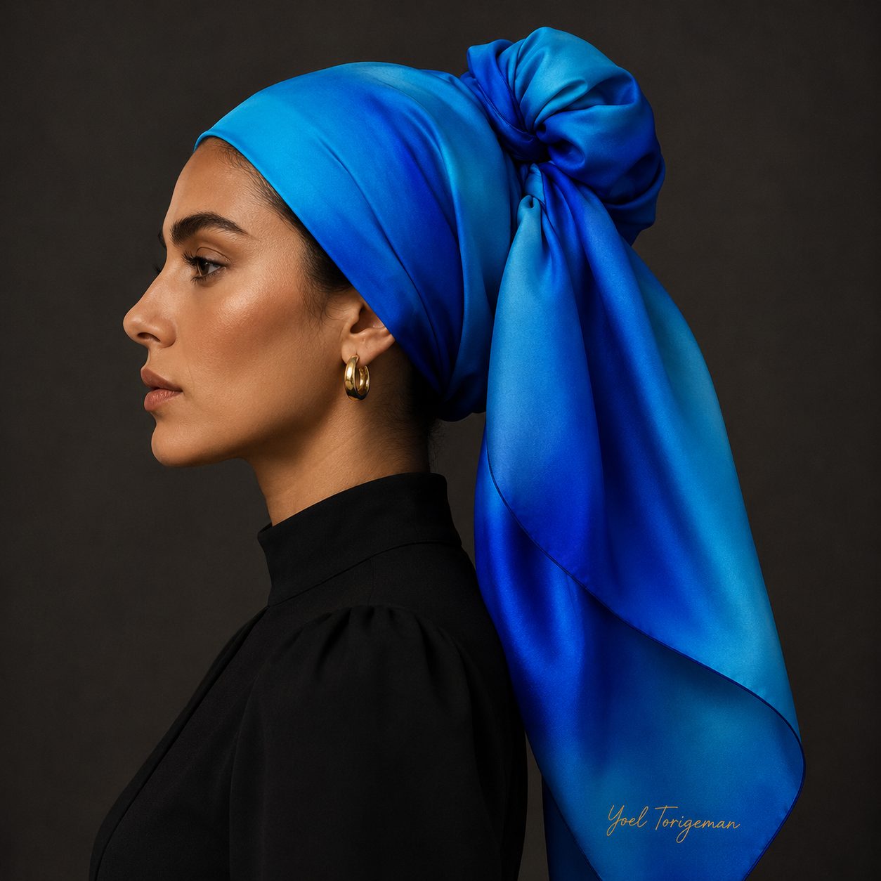 Model in profile wearing a cobalt silk art headscarf against deep black